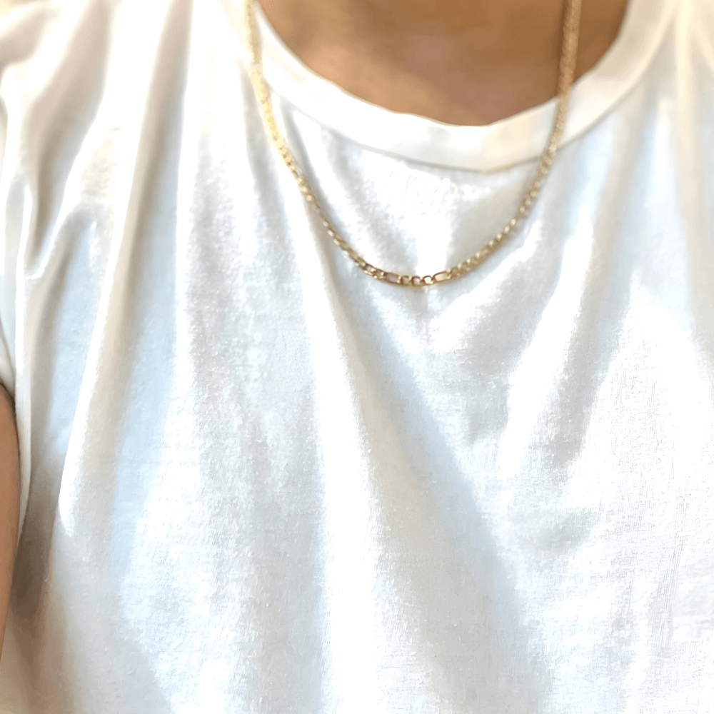 Close-up of a layered gold-filled Figaro chain necklace worn over a white shirt, showcasing elegant style.