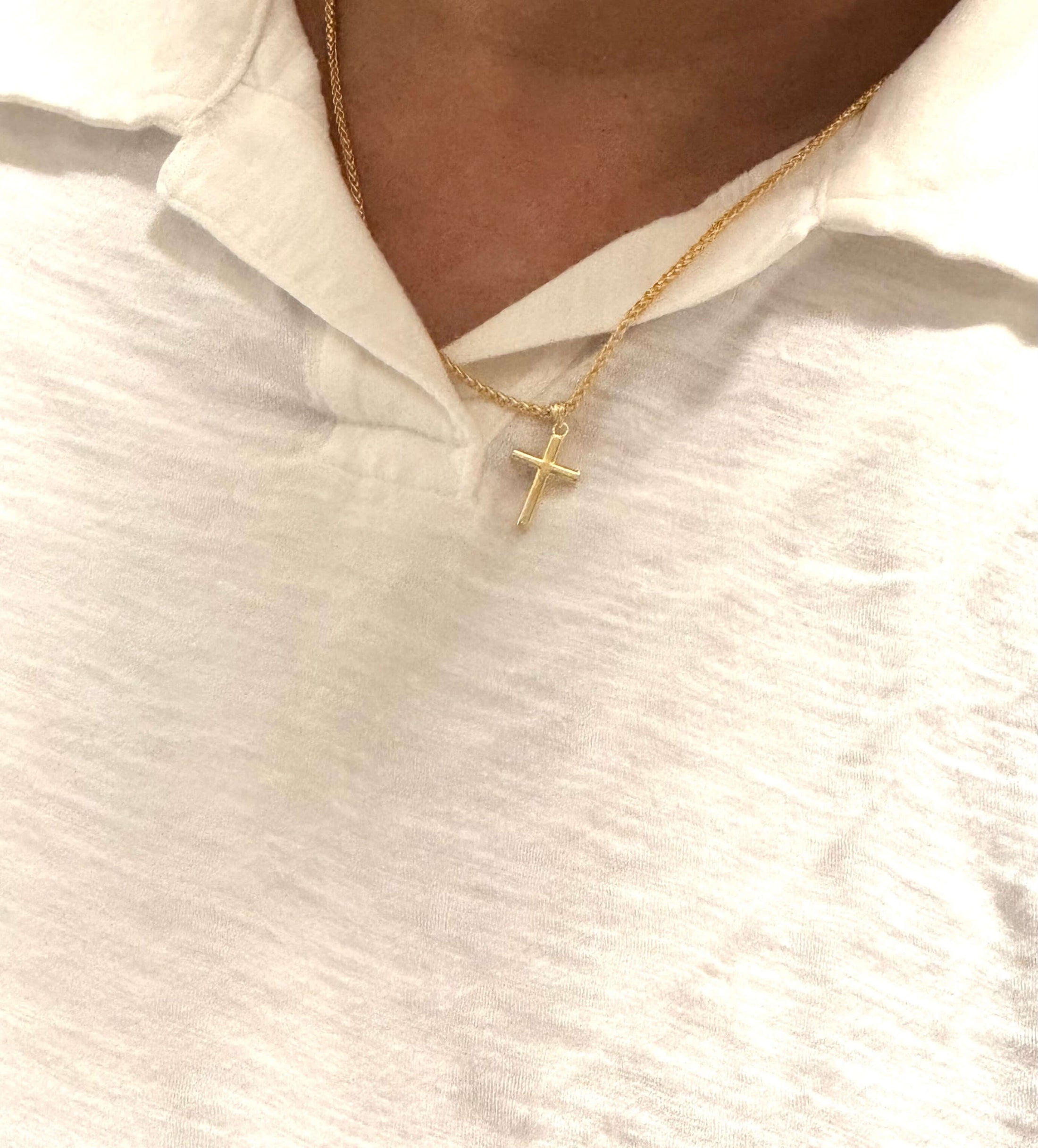 14K solid gold small cross pendant worn on a white polo shirt, showcasing timeless elegance and minimalist design.