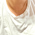 Load image into Gallery viewer, Close-up of a 24K gold-filled Figaro chain necklace worn on a white t-shirt, showcasing its elegance and design.
