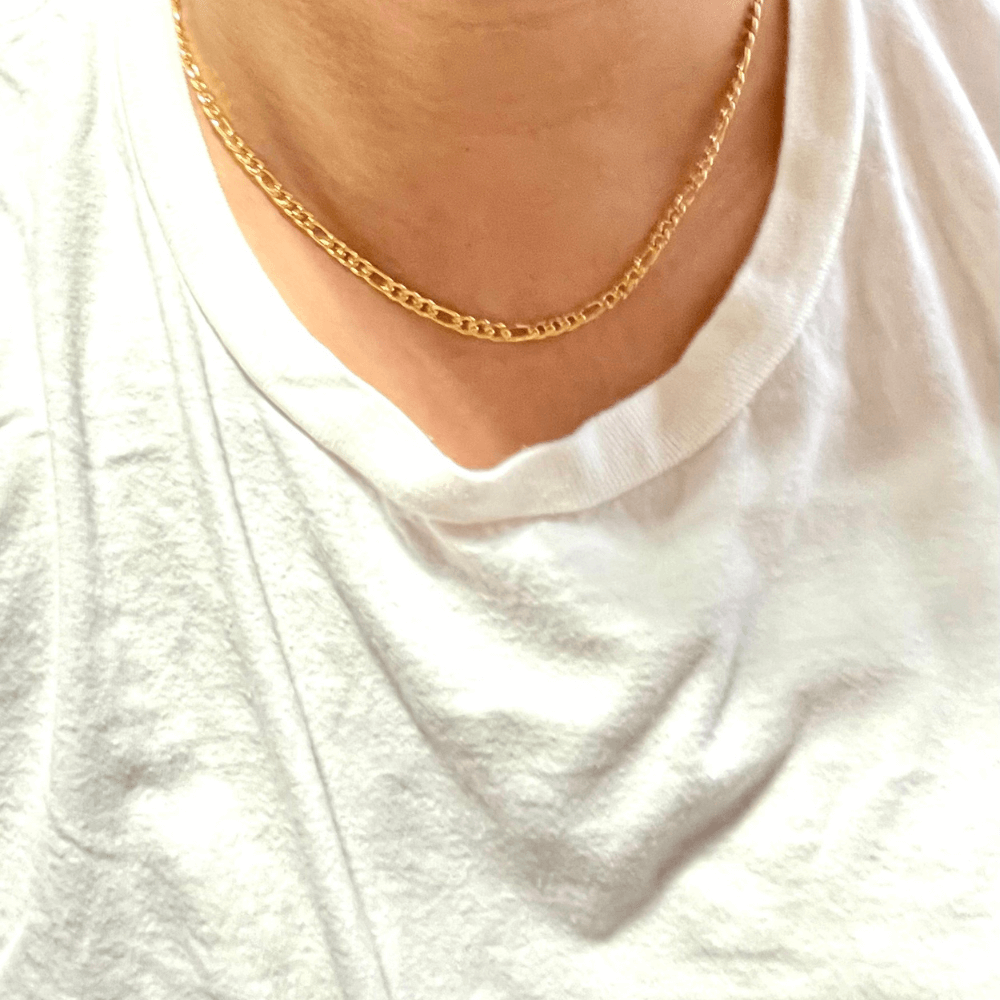 Close-up of a 24K gold-filled Figaro chain necklace worn on a white t-shirt, showcasing its elegance and design.