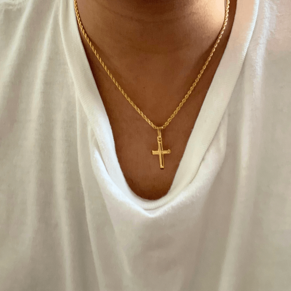 Gold-filled rope chain necklace with small cross pendant worn over a white shirt.