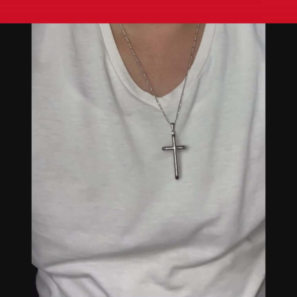 Person wearing a silver cross pendant necklace on a white t-shirt, showcasing a stylish accessory.